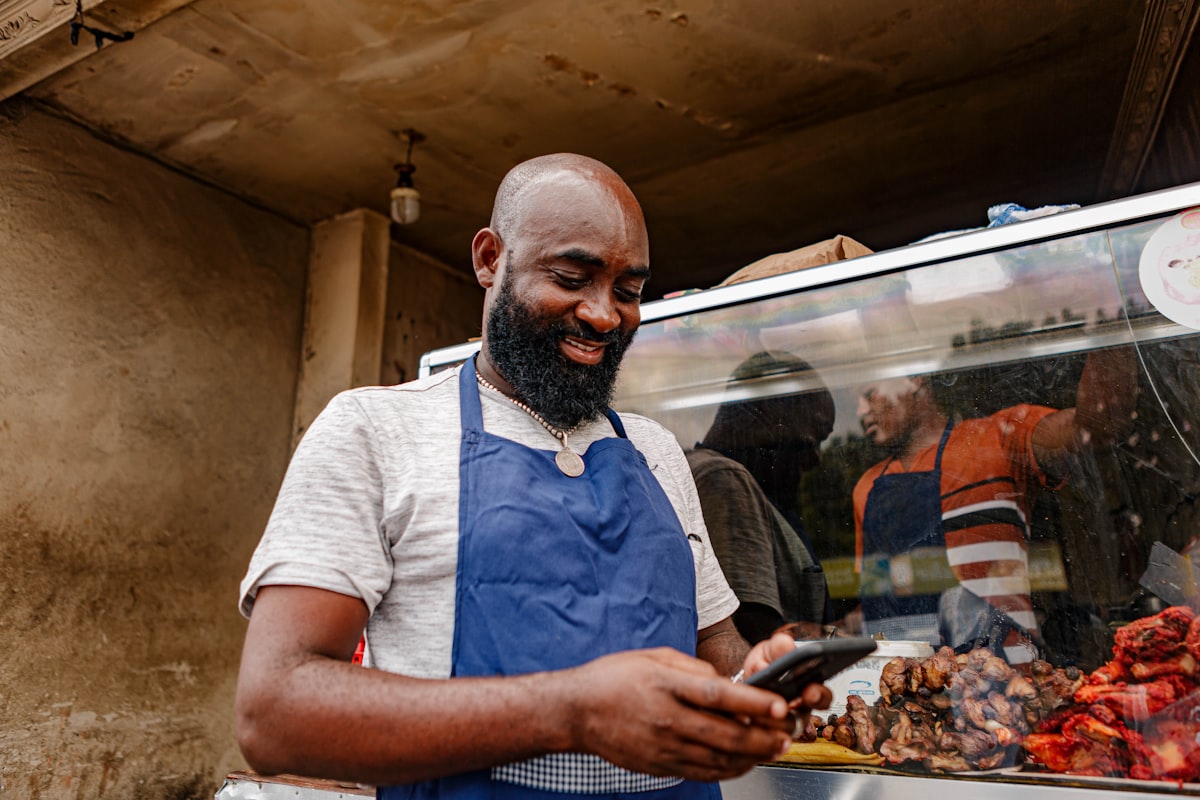 Vendedor de comida sonriendo mientras mira su celular en su puesto